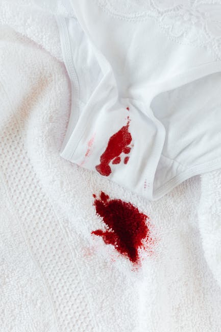 Close-up of a white fabric surface, possibly a bedsheet or towel, with a prominent bloodstain and a blood-saturated cloth partially visible in the upper left corner. The fabric appears clean but shows the impact of the fresh stain, indicating a need for stain removal and sanitisation. The setting suggests a domestic environment in need of surface cleaning for hygiene and stain management, emphasizing the importance of rapid deep cleaning. This image illustrates the type of emergency stain removal services offered by Mayfair Carpet Cleaners, who specialise in domestic cleaning and hygienic surface maintenance. The lighting is neutral and even, highlighting the contrast between the white fabric and the red stain, underscoring the importance of professional cleaning to restore surface cleanliness.