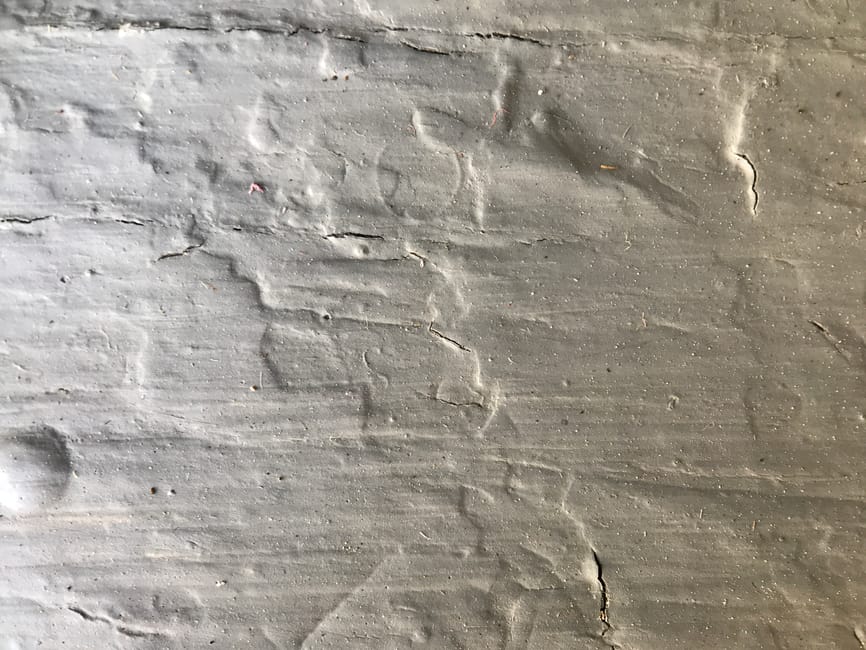Close-up image of a concrete or cement floor with visible cracks, water stains, and discoloration, indicating areas affected by moisture or leaks. The surface appears rough with uneven texture and some dust particles. The lighting highlights the surface’s natural color variations, emphasizing the need for deep cleaning and maintenance. This setting is typical of a basement or a low-light indoor space that has experienced leak-related issues. The image productively illustrates the importance of surface cleaning and sanitisation, as offered by Mayfair Carpet Cleaners, especially for addressing mould after leaks in basement environments, aligning with the page about quick fixes for mould after leaks in Mayfair basements.